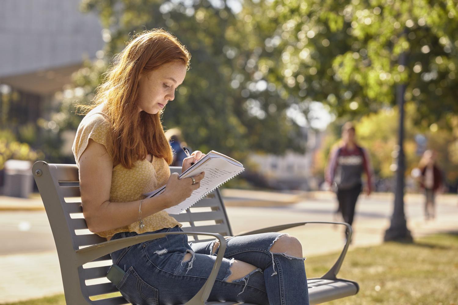 A <a href='http://zd6y.peakuniverse.com'>BETVLCTOR伟德登录</a> student reads on a bench along Campus Drive.